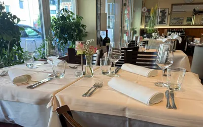 Eingedeckte Tische mit cremeweißen Stofftischdecken, gerollten Servietten und Weingläsern an der Fensterfront des Fellini